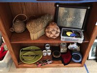 Full view of two shelves displaying the assortment of themed decor including woven baskets, crystal candleholder, sushi plates with chopsticks, sake cups, pottery items, felt items, salt cellar, and framed vintage map.
