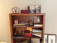 Wide view of wooden shelving holding assorted Asian themed decor including scrolls, figurines, serving tray, and boxed urn.