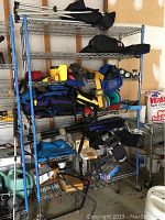 Full view of metal shelving unit with various gear: life vests, diving accessories, kayak carrier, pumps.