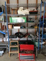 Full view of metal shelving unit with a collection of tools and sprayer. Craftsman red toolbox is open showing tools inside. Among tools are Black and Decker power tools and other hand and yard tools.