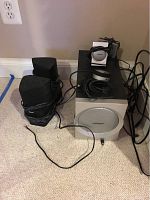 Full system showing two satellite speakers, subwoofer, and control unit placed on carpeted floor