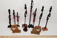 Wide shot of 9 African wood carvings including 6 tall figurines and 3 smaller sculptures, with measurement scale for size reference
