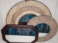 Three framed wall mirrors displayed against a wall showing various shapes and frame styles.