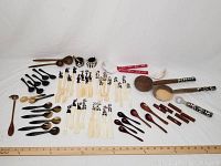 Wide view of all utensils showing lot contents including various spoons, bowls, and bottle opener on white background with measuring ruler.