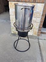 Full view of stainless steel turkey fryer pot on black metal stand outdoors on concrete