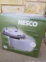 Front view of the green Nesco professional food and jerky dehydrator box, showing product image and key features like adjustable temperature control and top-mounted fan.