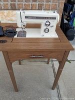 Kenmore sewing machine mounted on foldable wood grain table with drawer and metal handle, photographed from front.