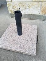 Top view of square granite base with attached black cylindrical umbrella pole.