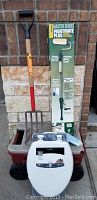 Photo of compost pitchfork with red handle next to Wagner Paintmate Plus roller kit box and white toilet seat in front of brick wall