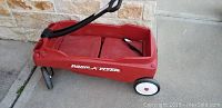Side view of the red Radio Flyer wagon showing the plastic body, black metal pull handle, and white wheels with red center caps.
