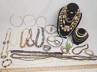 Wide view of multiple natural look jewelry pieces arranged on white surface and black busts, including necklaces, bracelets, and earrings