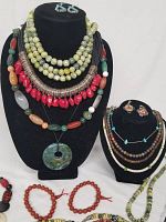 Front view of two display busts holding multiple layered gemstone necklaces and small pairs of earrings.