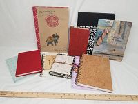 Full view of the 10 journals and notebooks arranged on a surface with a yardstick for scale.