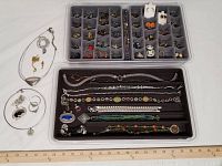 Full lot with two trays containing rings, multiple bracelets, and necklaces lying in one tray; additional necklaces and earrings positioned outside the trays.
