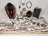 Wide view of all jewelry pieces laid out including necklaces, bracelets, earrings, rings, with black necklace stands and a small shelf for bracelets.