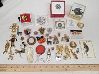 Entire collection of varied pins and brooches laid out on white cloth with measuring ruler below for scale.