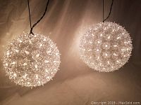Photo of two illuminated spherical light decorations suspended, showing detailed texture and warm glow.