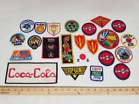 Wide view of all fabric patches arranged with a ruler for scale, showing many colorful embroidered and one beaded Coca-Cola patch.