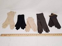 Five pairs of ladies gloves in beige, black, and brown laid flat next to a ruler to show size