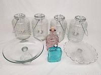 Lot of clear glassware including four lanterns with metal handles and tealight holders, two glass cake stands, and two decorative glass bottles with cork stoppers.