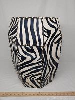 Front and side view of the zebra print storage stool showing the hexagonal shape and visible metal studs along the edges with a corner requiring repair.