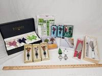 Variety of wine stoppers, cheese and cake knives, tea towels, and bottle openers arranged with packaging and ruler for scale