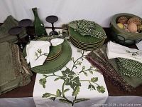All table linens, plates, napkins, candle holders, vase and oil warmer displayed together on a table with white backdrop.