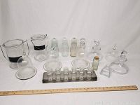 Full assortment of glassware items on white backdrop with ruler for scale