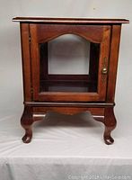 Front view of wood frame curio side table with glass door, showing brass knob and curved legs