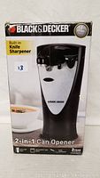 Box front showing Black & Decker 2-in-1 can opener with built-in knife sharpener, black and stainless steel design.