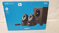 Boxed Logitech Z313 multimedia speaker system showing product image including two satellite speakers, subwoofer, and control pod with power rating 50W.