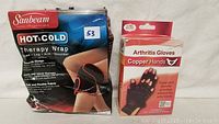 Photo of Sunbeam Hot & Cold Therapy Wrap package with distressed packaging and Copper Hands Arthritis Gloves box in front.