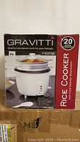 Front and side view of the box showing brand Gravitti, capacity 20 cups, and product image of white rice cooker with steam attachment.