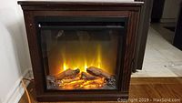 Front view of electric fireplace displaying glowing flame and log effects with red oak finish mantel.