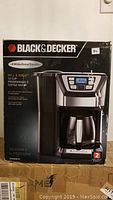 Front of box showing Black & Decker Mill & Brew 12-cup programmable coffee maker with digital controls and grinder feature. Indicates designed to perform and two-year warranty.