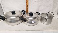 All three aluminum cooking pots with lids displayed side by side showing size variations and handles