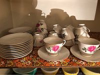 Set of white china cups and saucers with rose floral pattern, stacked and displayed on a floral cloth