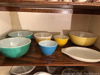 View of all 7 pieces: six bowls in varying colors and sizes with some scratches and chips, and one oval platter with green floral pattern on white base.