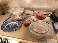Overview photo showing assorted plates, bowls, and glassware on stovetop including Staffordshire, Valmont China plates, and glass bowls.