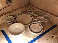 Overall view of all 18 pieces including plates, saucers, and mugs arranged on a kitchen counter corner.
