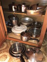 Cabinet shelf with assorted pots, pans, colanders, and sieves including enamel pot, metal bucket, mesh sieve