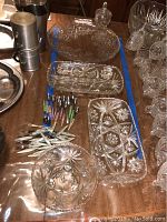 Photo showing five crystal serving pieces on a wooden surface with over 20 hors d'oeuvre forks and spoons laid out beside them