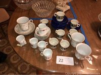 Photo of over 12 cups and over 15 saucers from three different sets arranged on a wooden table.
