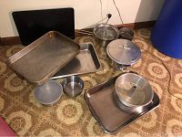 View of large rectangular baking pans and metal pot with lid on floor with other pans and kitchenware items