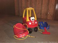 Red and yellow Little Tikes toy car with two tree swings, one red and one blue, with yellow ropes, displayed on floor against wooden wall.