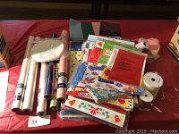 Wide view of the lot showing multiple rolls of wrapping paper, ribbon, and tape against a red background.