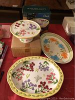 Cake plate on pedestal with floral embossed design on top and floral butterflies, next to its original box.