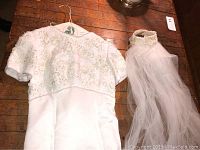 White short sleeve wedding dress with intricate beading on bodice and sleeves, hanging on a hanger on a wooden floor.
