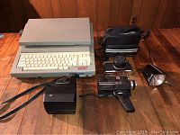 Pentax K1000, Instamatic M18 movie camera, Polaroid Sun660, Brother Word Processor WP 760D grouped on wooden floor.