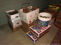 Boxes filled with over 50 glass mason jars and other large jars. Some boxes are produce boxes and one contains a white bucket with jar lids.